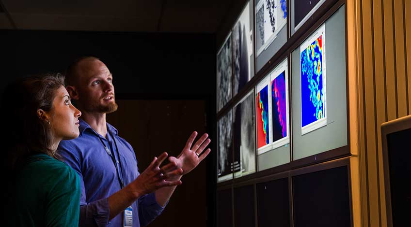 Two researchers discuss images on an illuminated wall.