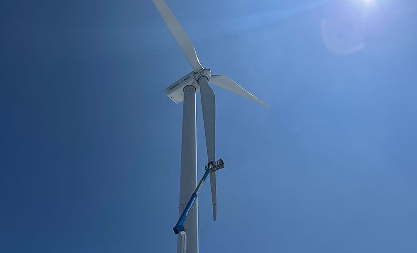 20240723-newsletter-wind-turbine A worker in an extended aerial lift works on the blade of a wind turbine