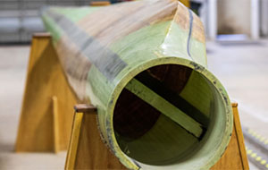 The hollow interior is seen from the end of a horizontal wind turbine blade resting on wooden supports.