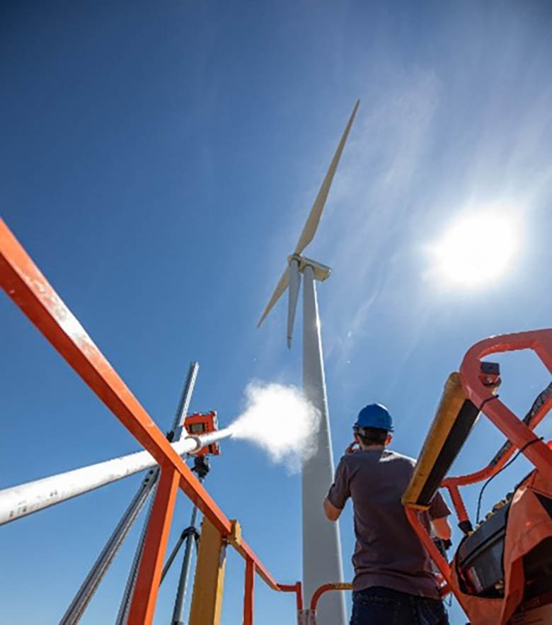 A researcher stands next to a pneumatic launcher, which fires a projectile at a wind turbine