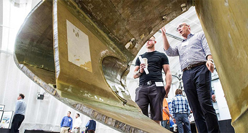 Two scientists stand  behind a large section of a printed blade mold.