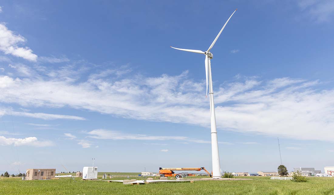 A small wind turbine next to a crane, small building, and equipment.