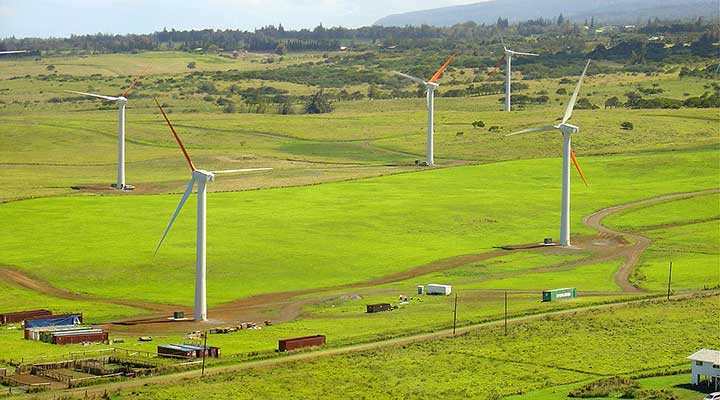 An aerial photo of five land-based wind turbines in a green field.