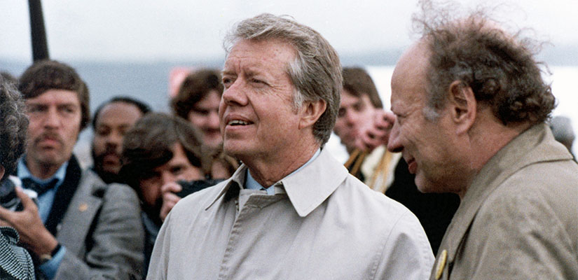 Two people standing together with others holding cameras behind them.