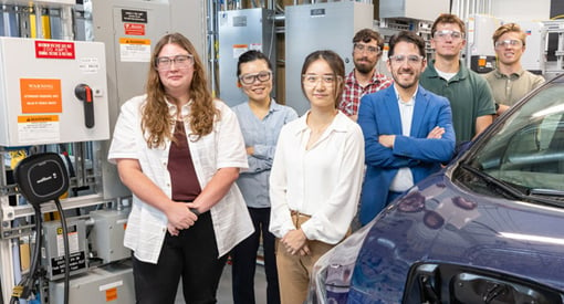 SSeven people pose alongside a vehicle in a laboratory.