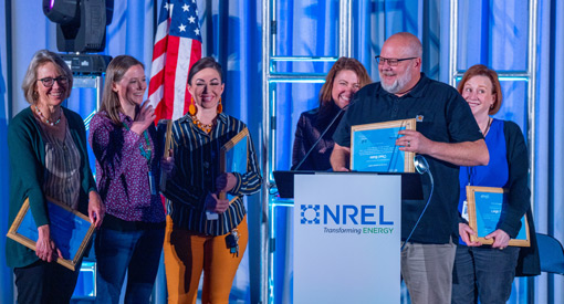 A person holding a plaque while standing behind a podium, surrounded by smiling people.