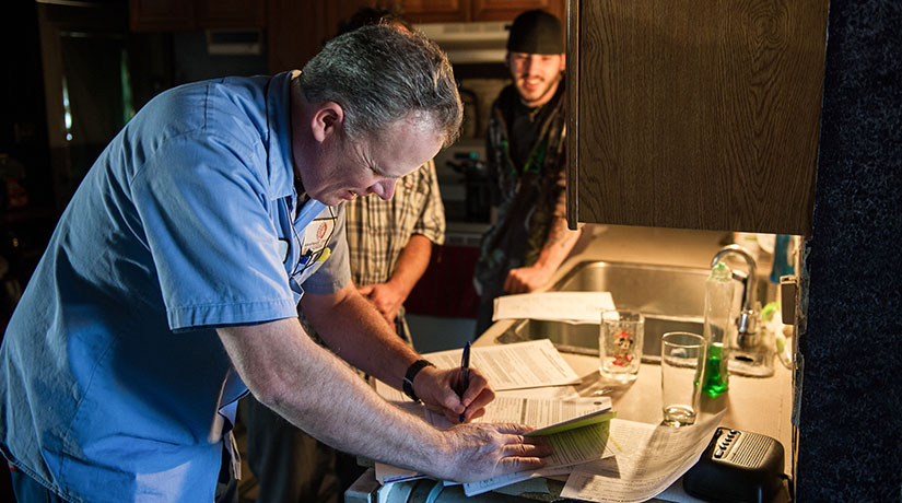 A man signing papers while people watch.