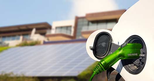 Close up view of Electric Car charging and houses with solar panels in the background