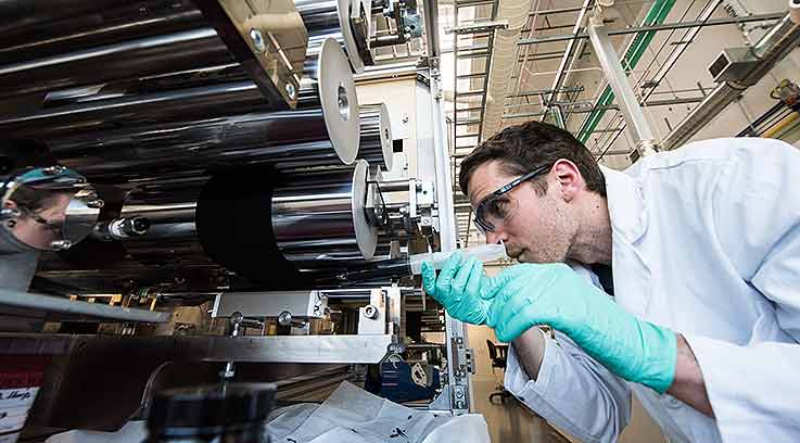 A person in a lab wearing eye and hand protection places a plastic object into a machine.