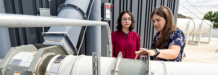 A mentor works with an intern on an outdoor piece of equipment.