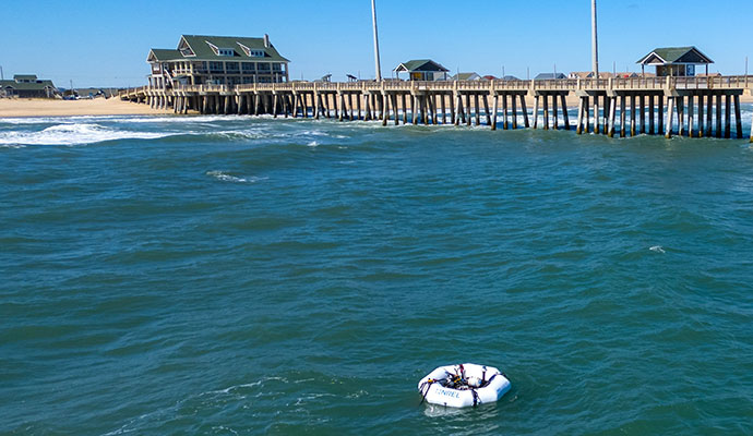 Wave energy converter device floats in ocean next to pier