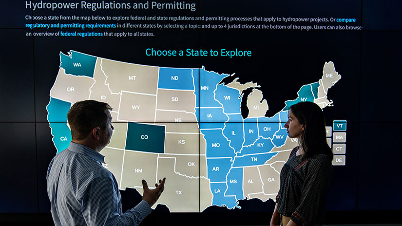 Two researchers discuss in front of data displayed on large screen