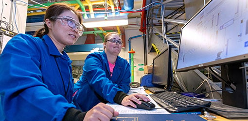 Two people look at a computer monitor while wearing safety glasses.