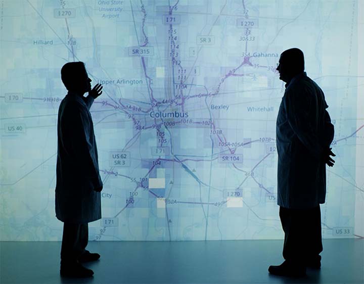 2018-09-photo-02 Two researchers stand in front of a blue-green raod map of Columbus, Ohio, in NREL's visualization room.