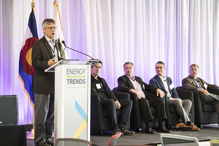 2018-09-photo-05 A man speaks at a podium that says Energy Innovation Trends, in front of the Colorado flag. Four other men seated behind him listen to the presentation.