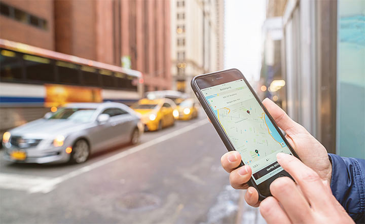 7-201806-thsc-680745636 A person uses a ride-hailing app on their phone to order a ride in a city